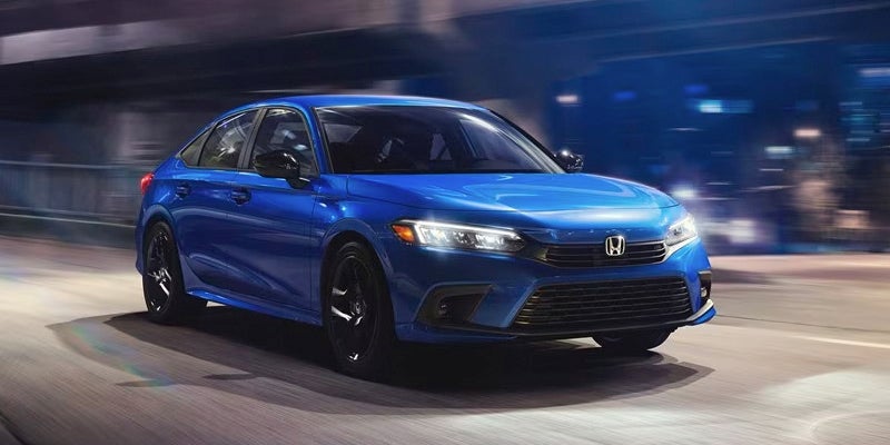 A photo of a blue 2024 Honda Civic Sedan driving down a street at night.