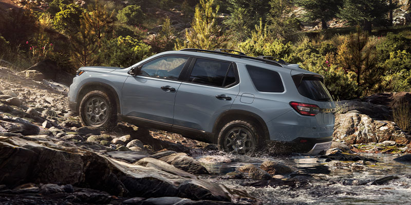 A photo of a gray 2025 Honda Pilot driving up a hill