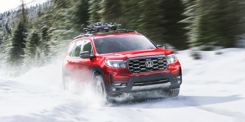 A red 2025 Honda Passport driving through snow.