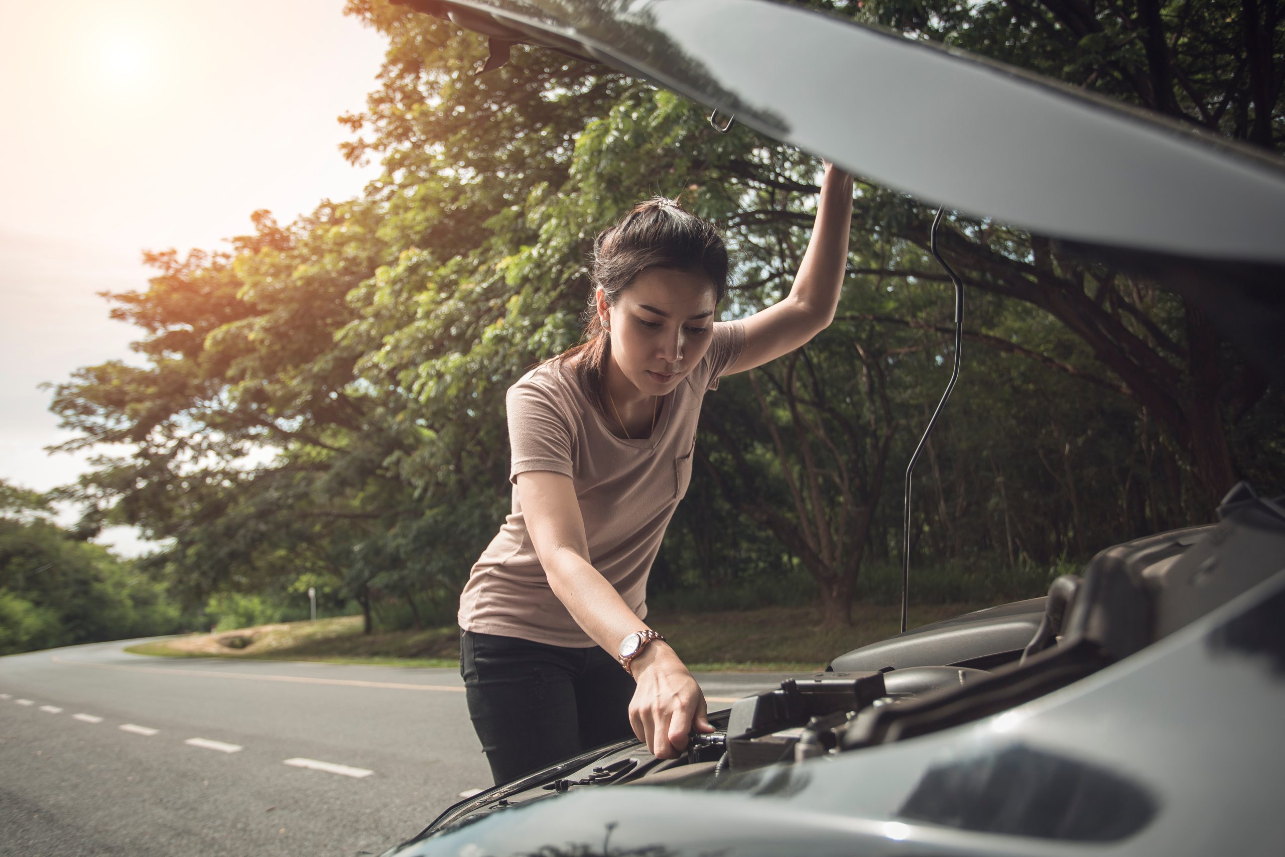 A woman looking at her car's engine on the side of the road